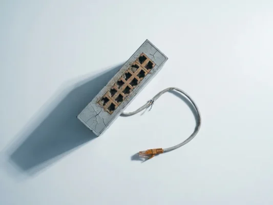 Verouderde netwerkswitch met gecorrodeerde poorten en losse ethernetkabel op wit oppervlak, bovenaanzicht.