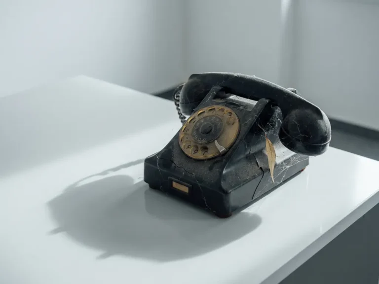 Verouderde gebarsten telefoon met spinnenwebben op modern wit bureau, zachte zijdelingse belichting, minimalistische compositie.